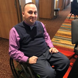 Man smiling in wheelchair with purple shirt.