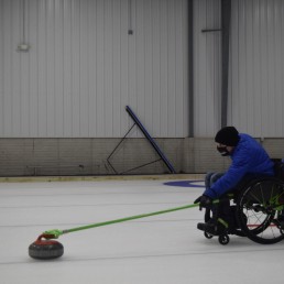 Man in wheelchair on the ice rink, practicing curling.
