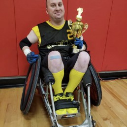 Man in wheelchair holding a gold trophy after playing basketball.