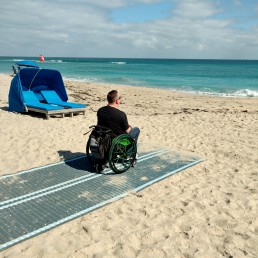 Man in wheelchair on the beach, sitting on a sand mat.