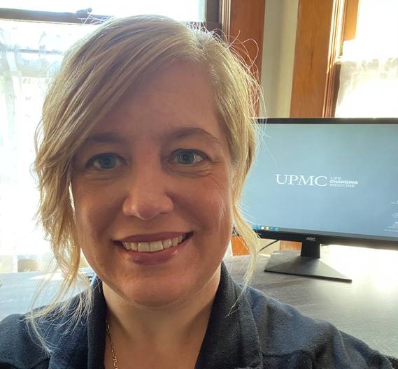 Woman smiles in front of computer screen.