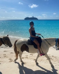 Woman riding white and brown horse on beach.